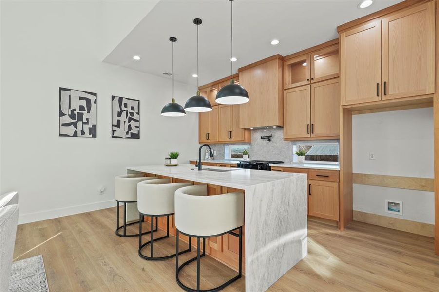 Kitchen featuring light stone countertops, a breakfast bar area, light wood-style floors, and decorative backsplash