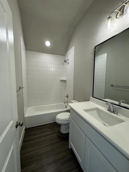 Full bathroom featuring vanity, lofted ceiling, tiled shower / bath, hardwood / wood-style flooring, and toilet