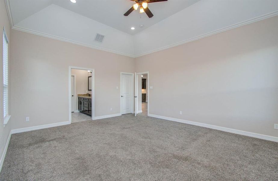 This is a spacious room with high ceilings, carpeted flooring, and neutral wall paint. It features a ceiling fan and multiple doorways leading to other parts of the home. The room is well-lit with natural light from windows.