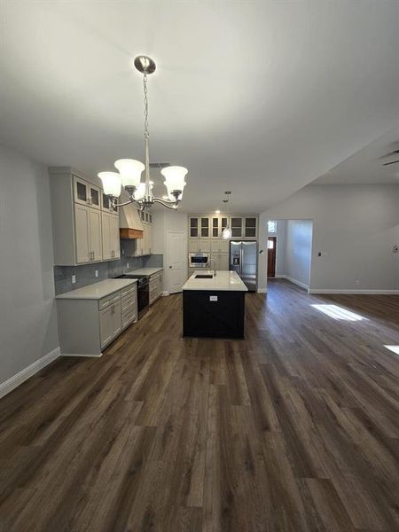 Kitchen with dark hardwood / wood-style floors, backsplash, a kitchen island, hanging light fixtures, and a notable chandelier