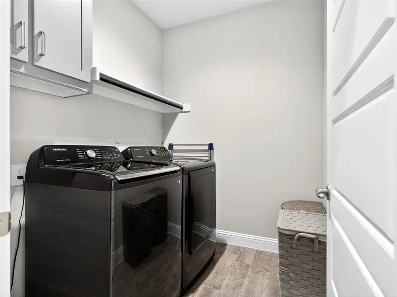 Laundry area featuring wood-finish flooring, white baseboards, and light gray walls Laundry area featuring wood-finish flooring, white baseboards, and light gray walls
