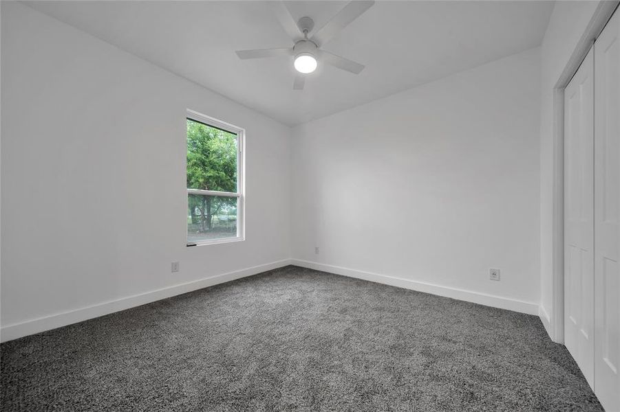 Unfurnished bedroom featuring ceiling fan, dark carpet, and a closet