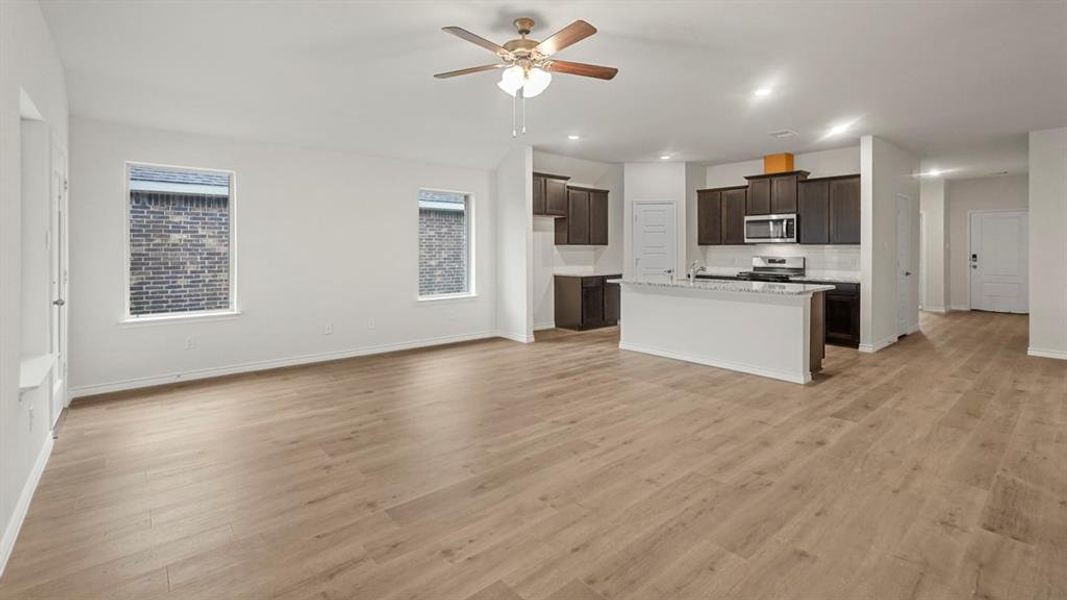 Kitchen featuring open floor plan, an island with sink, a ceiling fan, dark brown cabinetry, and light wood-style floors Kitchen featuring open floor plan, an island with sink, a ceiling fan, dark brown cabinetry, and light wood-style floors
