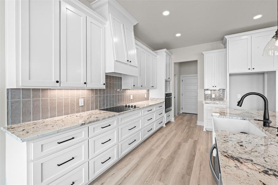 Kitchen featuring decorative backsplash, white cabinets, light stone counters, light wood-style flooring, and recessed lighting