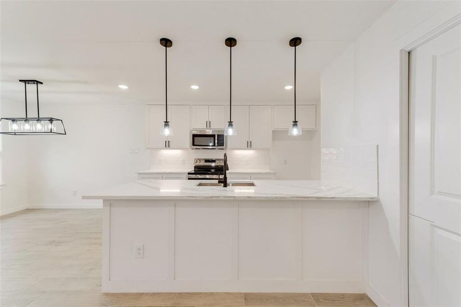 Kitchen with sink, pendant lighting, stainless steel appliances, light stone countertops, and white cabinets