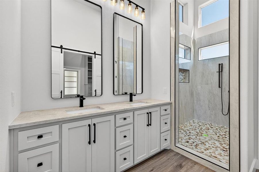 Bathroom featuring double vanity, a marble finish shower, and wood finished floors