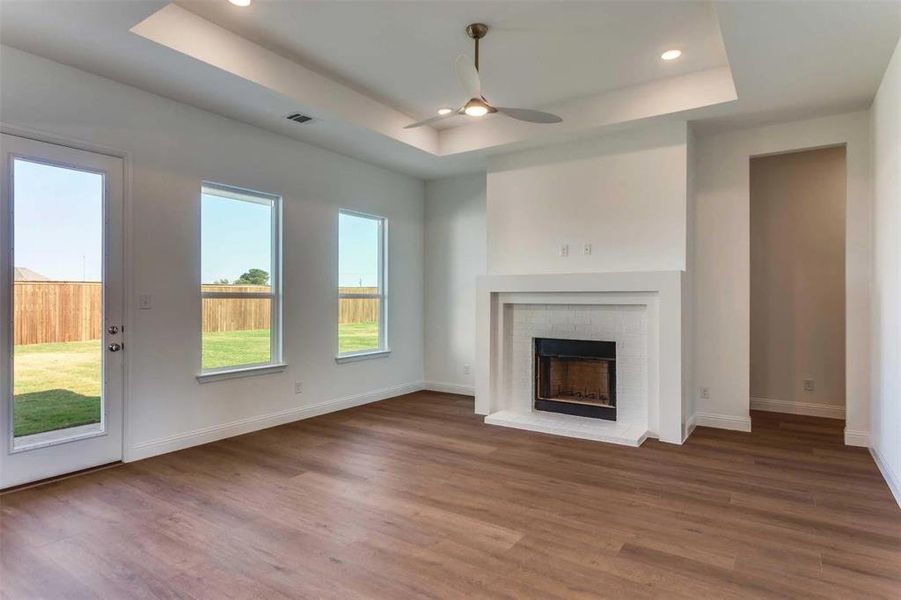 Unfurnished living room with a tray ceiling, wood finished floors, a fireplace, recessed lighting, and ceiling fan Unfurnished living room with a tray ceiling, wood finished floors, a fireplace, recessed lighting, and ceiling fan