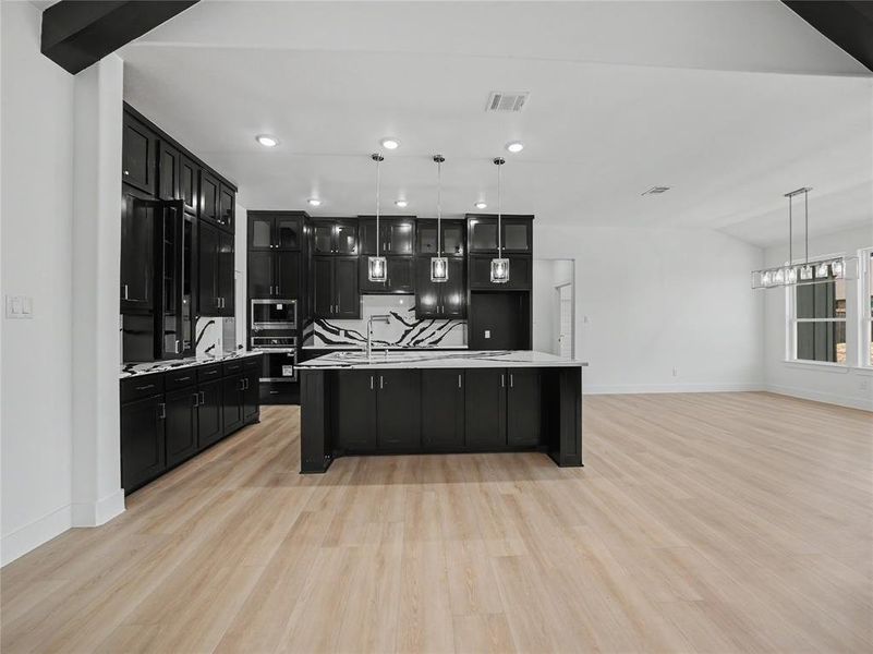 Modern kitchen featuring dark cabinetry, a central island with a sink, white countertops, and a patterned backsplash Modern kitchen featuring dark cabinetry, a central island with a sink, white countertops, and a patterned backsplash