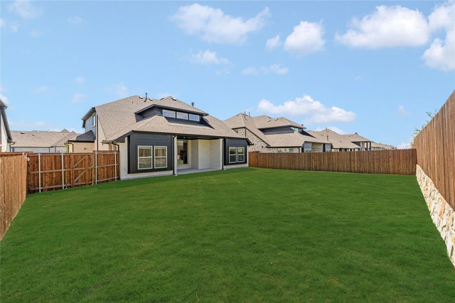 Backyard with large green lawn, covered patio, and wood privacy fence surrounding the home's rear exterior.