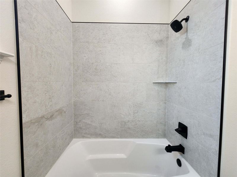 Bathtub with light-toned tiled surround, featuring a matte black shower head and faucet