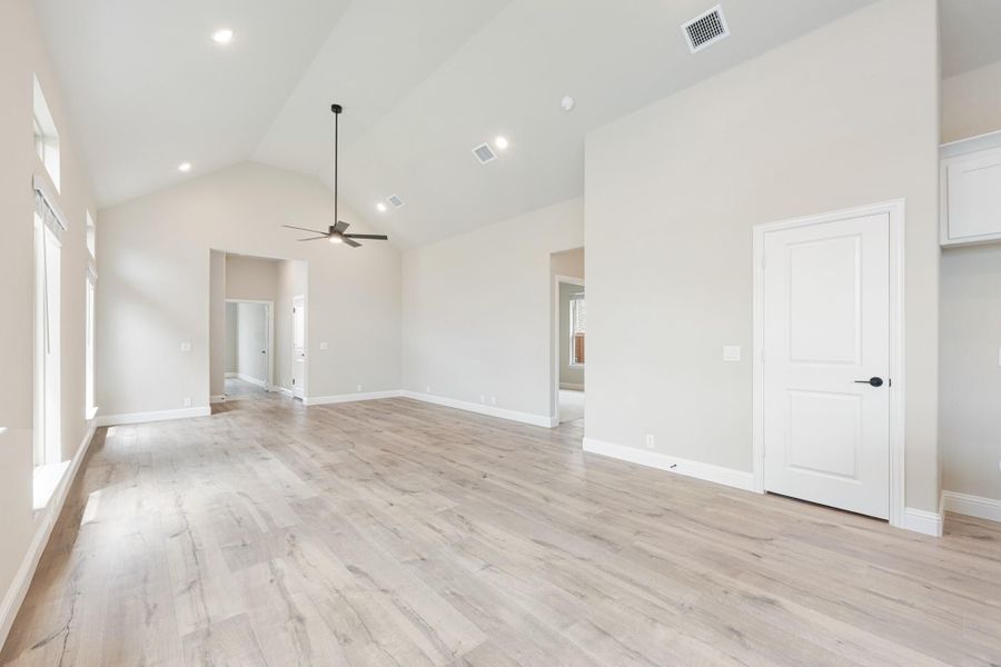 Empty living room with vaulted ceiling, ceiling fan, and light hardwood floors