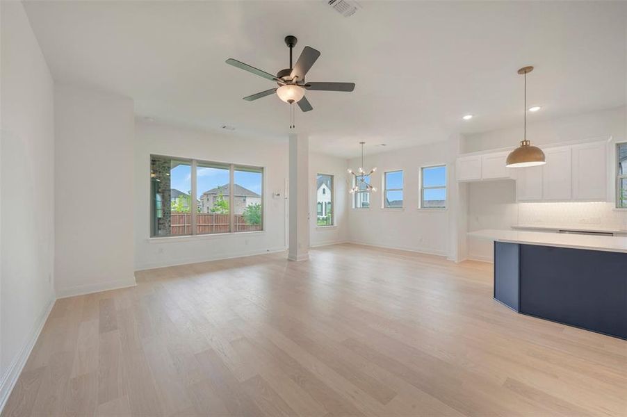 Expansive open-concept living space featuring light wood-finish flooring, a contemporary ceiling fan, and large windows providing abundant illumination