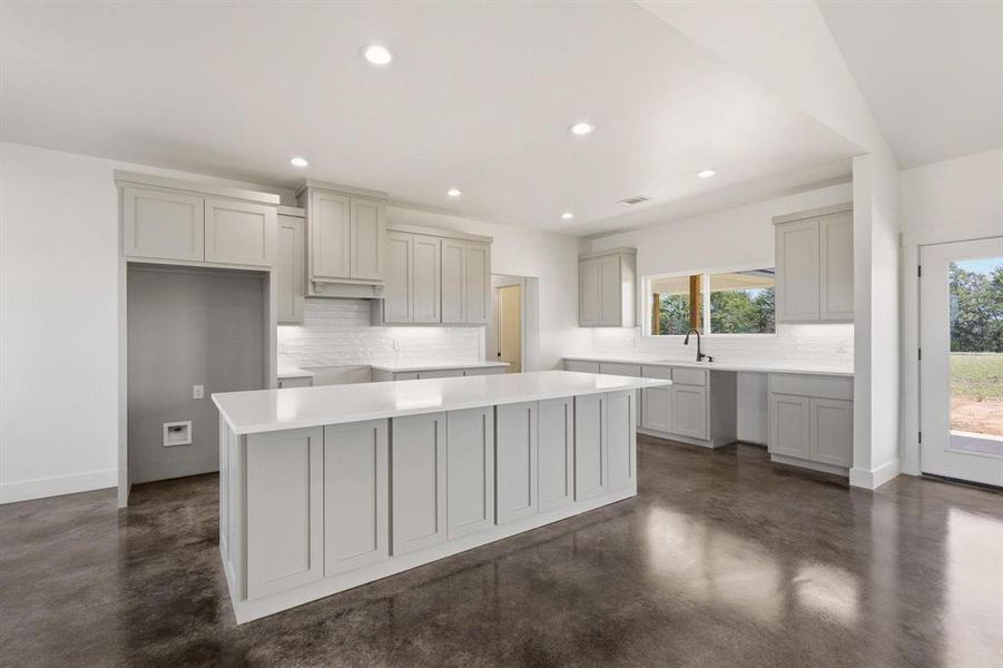 The spacious kitchen features light grey cabinetry, a large kitchen island with a white countertop, and white subway tile backsplash