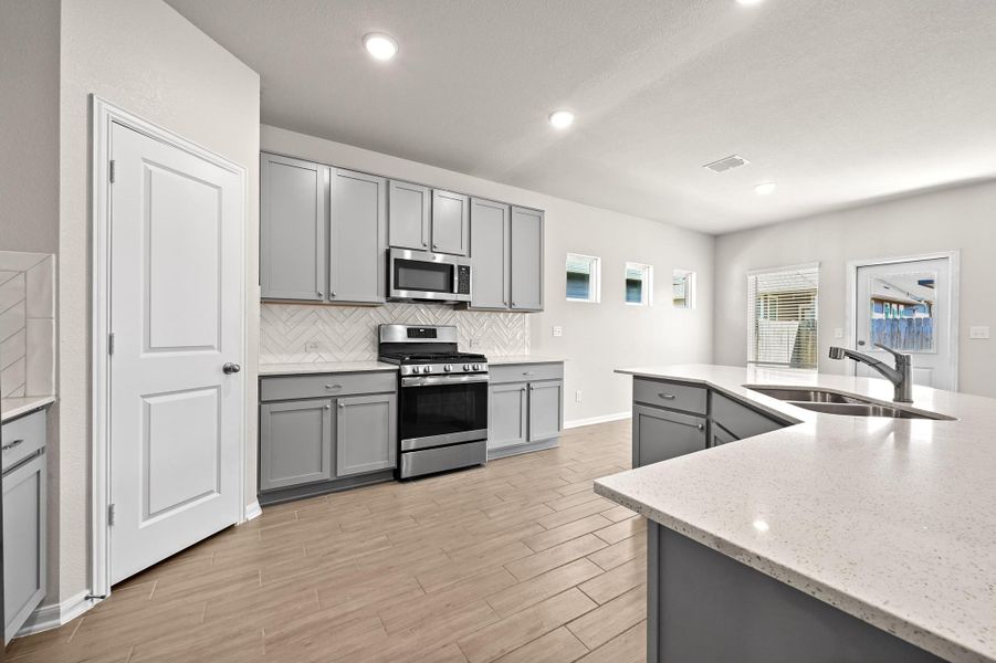 Kitchen with gray cabinets, stainless steel appliances, wood tiled floors, tasteful backsplash, and light stone counters