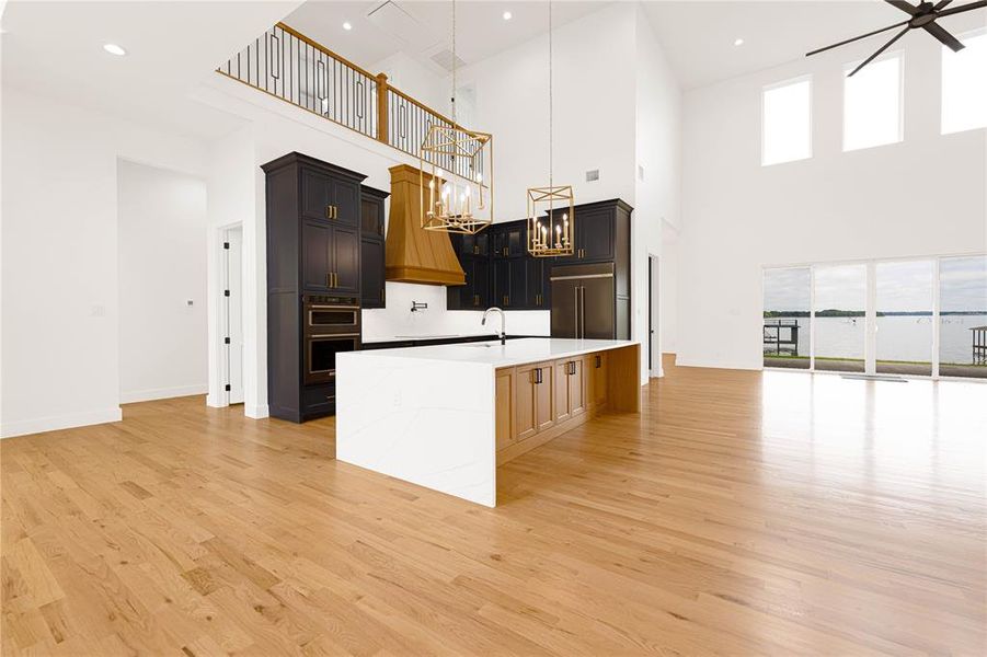 Kitchen with light stone counters, a kitchen island with sink, a chandelier, open floor plan, and double wall oven