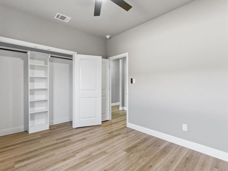 Unfurnished bedroom featuring a barn door, light wood-style flooring, a ceiling fan, and a closet Unfurnished bedroom featuring a barn door, light wood-style flooring, a ceiling fan, and a closet
