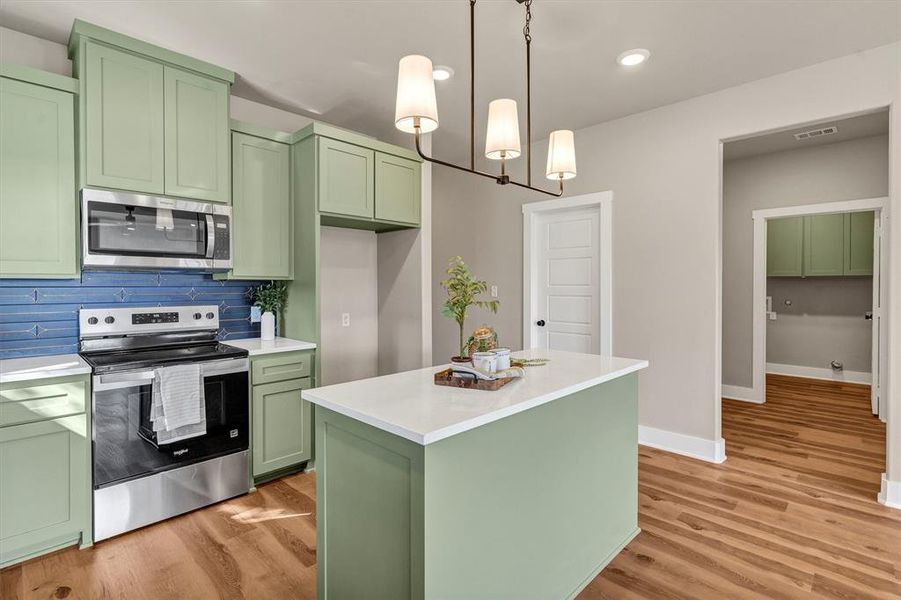 Kitchen featuring green cabinets, appliances with stainless steel finishes, decorative backsplash, light wood-type flooring, and hanging light fixtures Kitchen featuring green cabinets, appliances with stainless steel finishes, decorative backsplash, light wood-type flooring, and hanging light fixtures