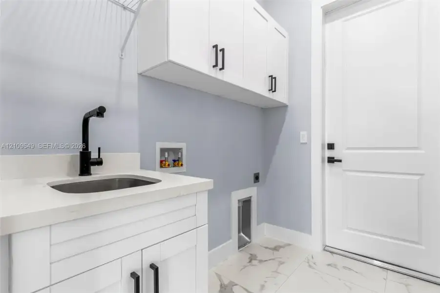 Utility area featuring shaker-style white cabinetry, stone-finish countertops, an undermount sink with a matte black faucet, and large-format tile flooring
