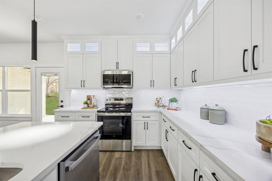 Kitchen with white cabinets, stainless steel appliances, dark wood-style floors, light stone counters, and backsplash