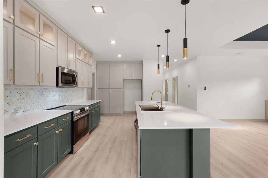 Kitchen featuring green cabinetry, appliances with stainless steel finishes, a sink, light wood-type flooring, and tasteful backsplash