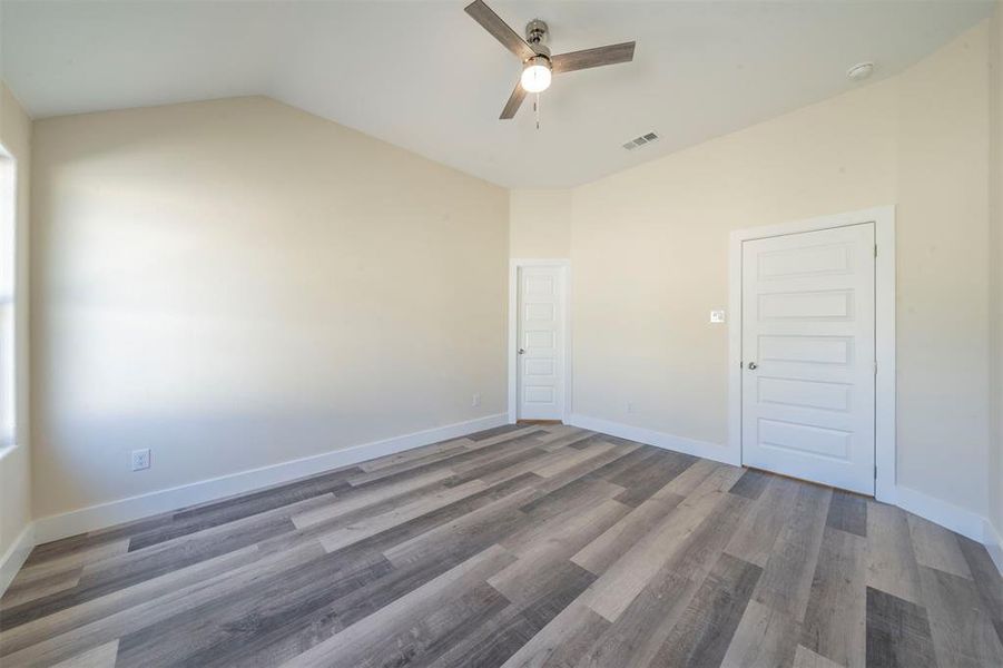 Unfurnished room with ceiling fan, lofted ceiling, wood finished floors, visible vents, and baseboards