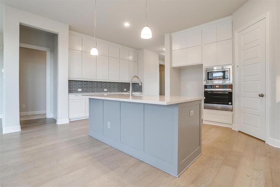 Kitchen with stainless steel microwave, light hardwood / wood-style flooring, white cabinets, decorative backsplash, and wall oven