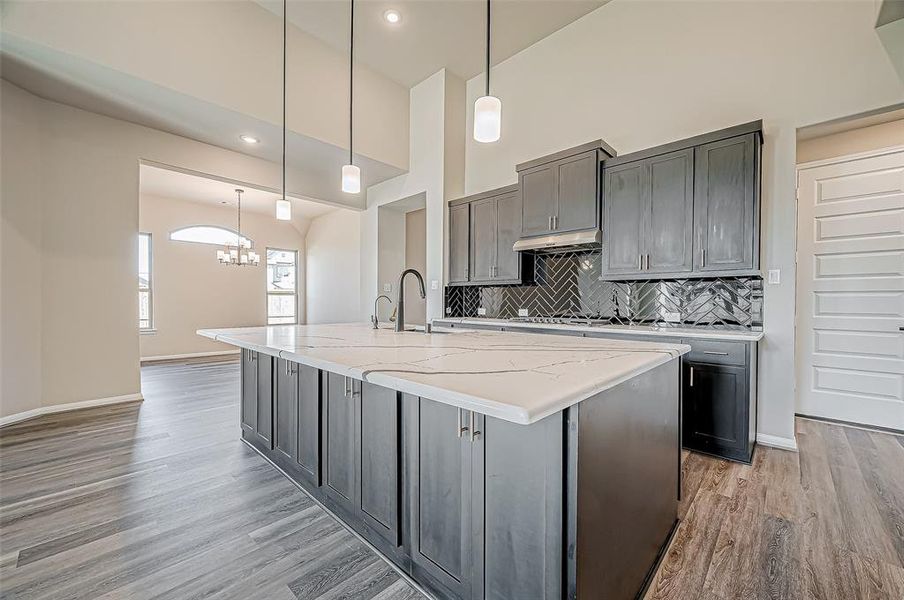 The chef’s kitchen is a true centerpiece, featuring a large extended island with dark granite countertops, upgraded cabinetry with gold hardware, a black hexagon subway tile backsplash, built-in stainless steel appliances, a 5-burner gas range, and a walk-in pantry.