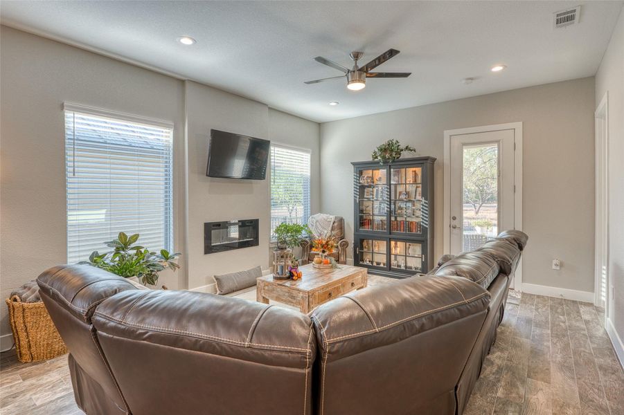 Living area featuring wood finished floors, ceiling fan, recessed lighting, and a glass covered fireplace
