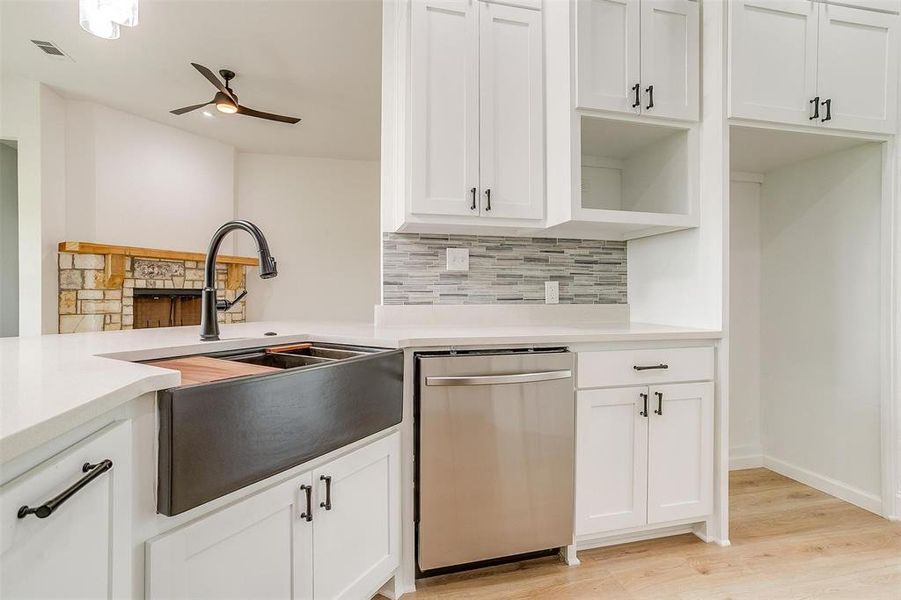 Kitchen featuring ceiling fan, backsplash, white cabinetry, stainless steel dishwasher, and light hardwood / wood-style flooring Kitchen featuring ceiling fan, backsplash, white cabinetry, stainless steel dishwasher, and light hardwood / wood-style flooring