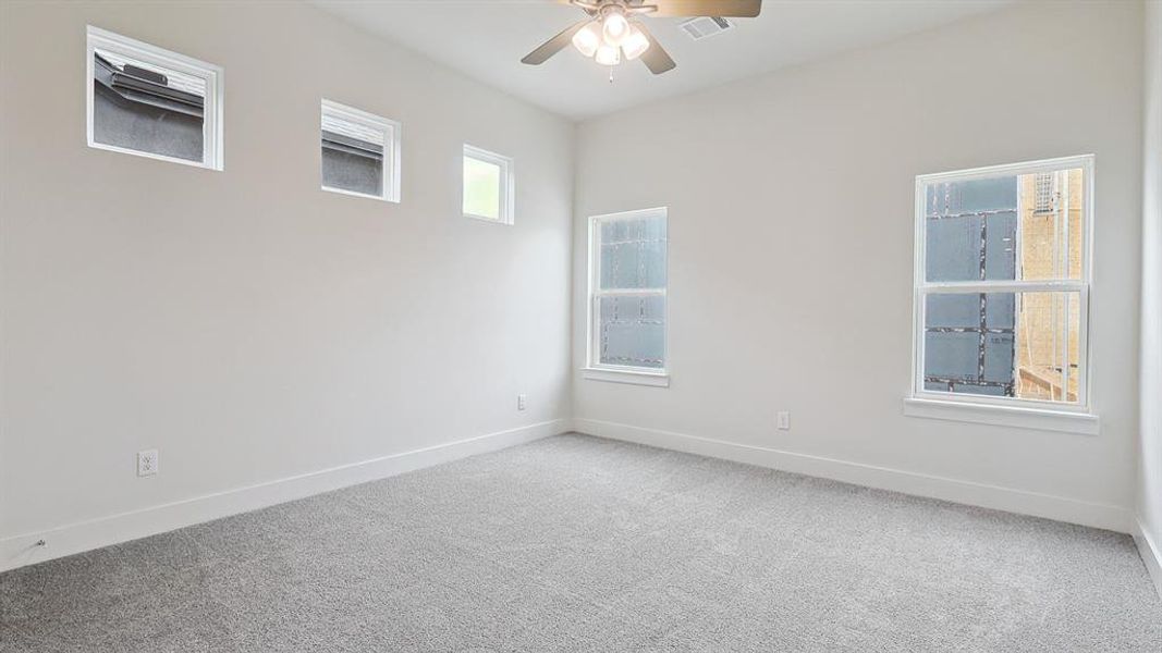 Spacious room featuring light gray carpeting, multiple windows, high ceilings, and a ceiling fan with integrated lighting