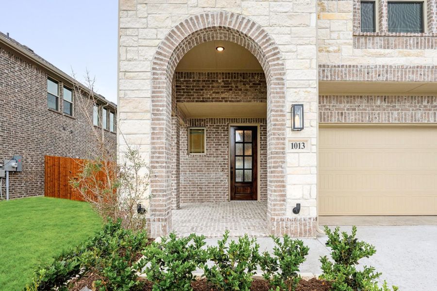 Home entrance with stone arch, brick facade, wood front door, and attached garage at address 1013