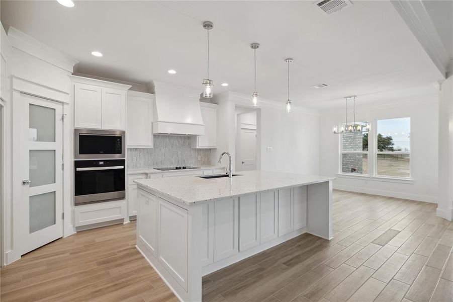 Kitchen featuring tasteful backsplash, stainless steel appliances, sink, light wood-type flooring, and custom range hood