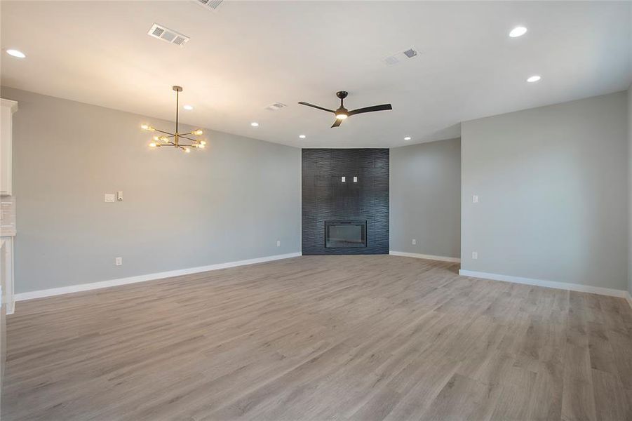 Unfurnished living room featuring a large fireplace, ceiling fan with notable chandelier, and light hardwood / wood-style flooring