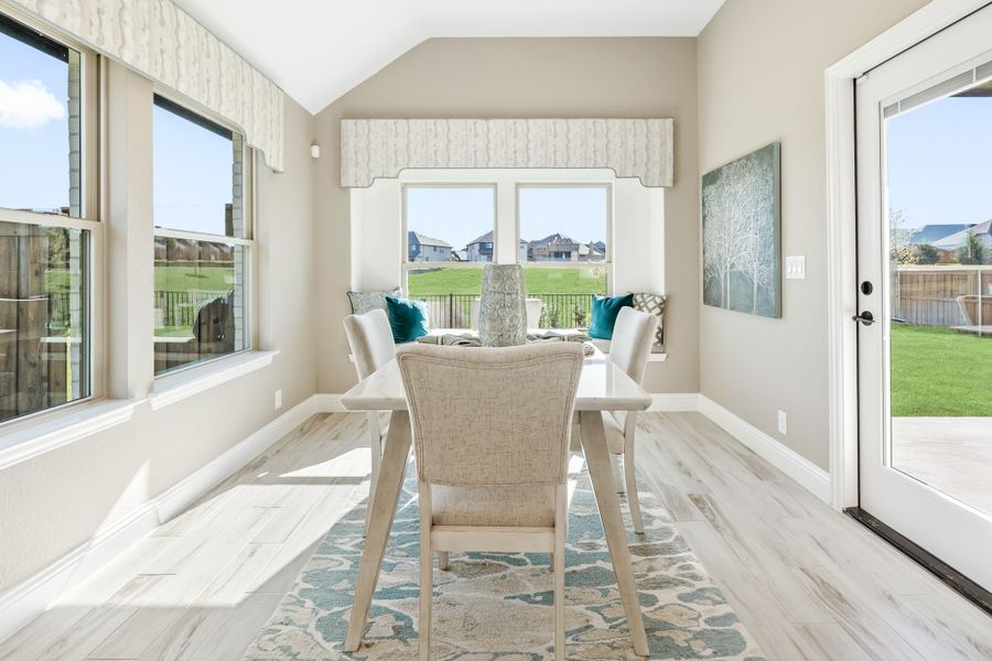Bright dining area with vaulted ceiling, white table, built-in bench seating, and large windows overlooking backyard