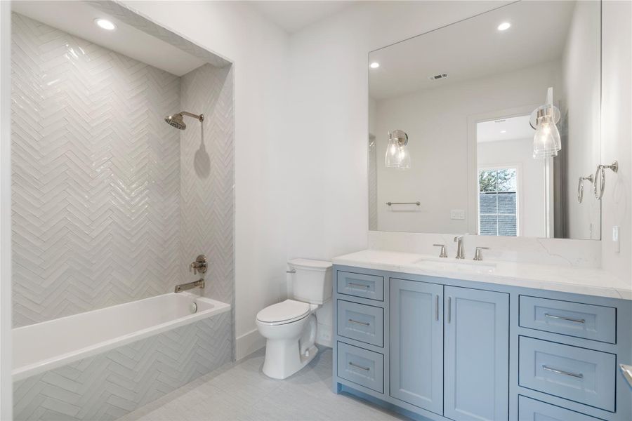 The en suite bathroom is decorated with white, glossy tiles in a herringbone pattern. Polished nickel fixtures continue, along with the lighter  gray tones of the vanity. The countertop and storage space is endless!