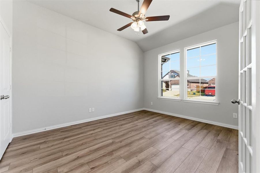 Spare room with light wood-style floors, vaulted ceiling, and a ceiling fan