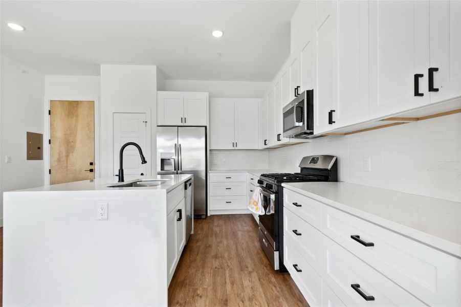 Kitchen with stainless steel appliances, light stone countertops, a center island with sink, white cabinetry, and recessed lighting