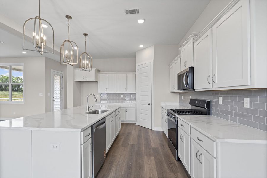 Kitchen with appliances with stainless steel finishes, white cabinets, pendant lighting, light stone countertops, and an island with sink