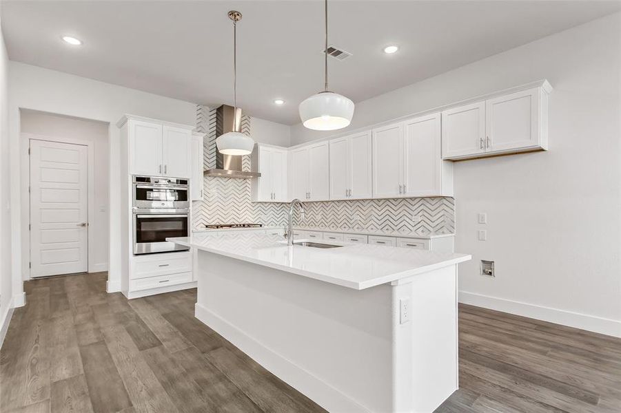 Kitchen featuring white cabinets, stainless steel double oven, an island with sink, and sink