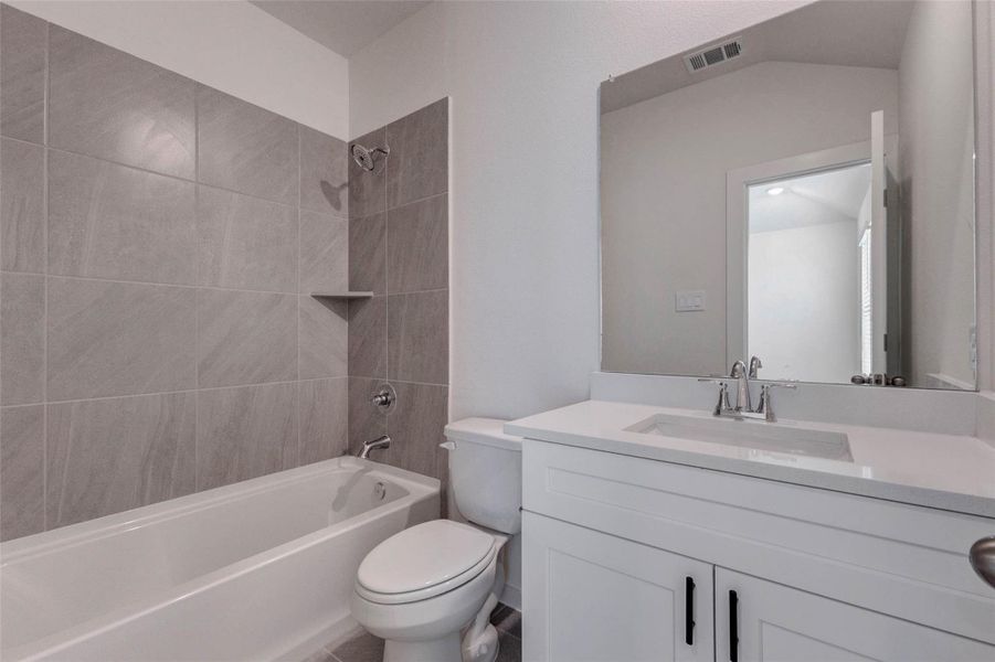 Full secondary bath featuring a white vanity, quartz-style countertop, large mirror, tub/shower combination, gray tile surround, and black cabinet hardware. The clean neutral palette feels fresh and modern, while the practical layout offers everything needed for guests or secondary bedrooms in a bright, low-maintenance space. Full secondary bath featuring a white vanity, quartz-style countertop, large mirror, tub/shower combination, gray tile surround, and black cabinet hardware. The clean neutral palette feels fresh and modern, while the practical layout offers everything needed for guests or secondary bedrooms in a bright, low-maintenance space.