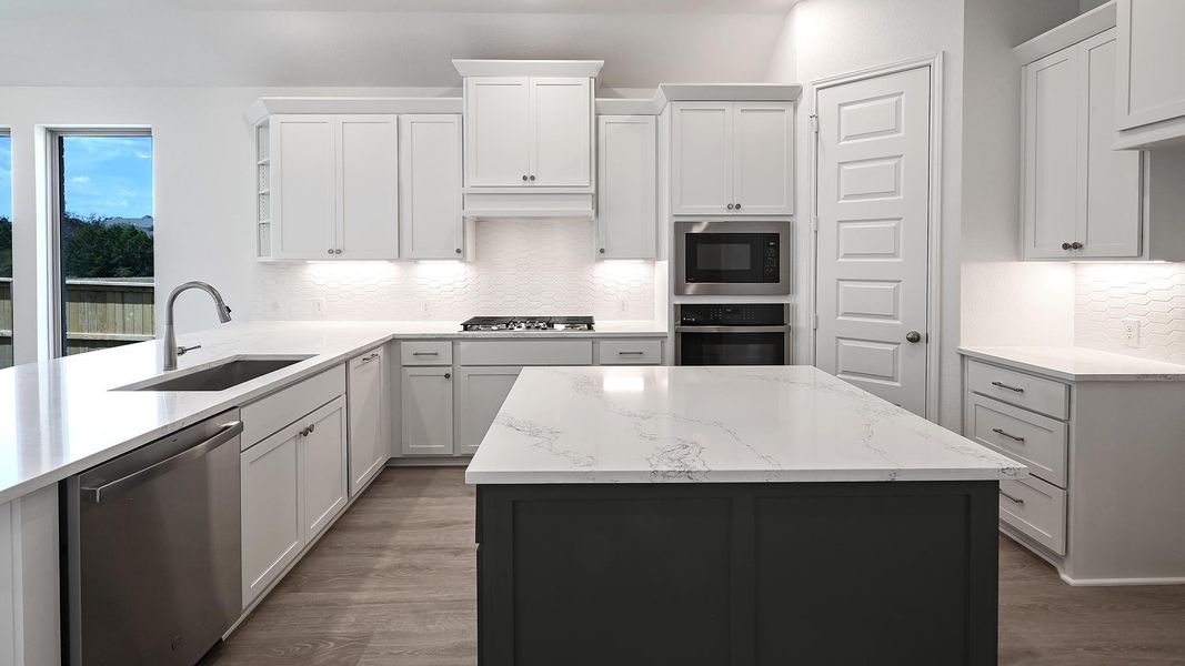 Kitchen featuring backsplash, a center island, light stone counters, and appliances with stainless steel finishes Kitchen featuring backsplash, a center island, light stone counters, and appliances with stainless steel finishes