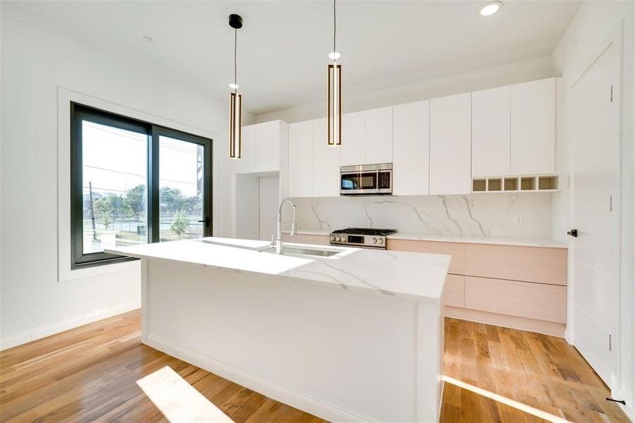 Kitchen with white cabinets, an island with sink, light wood-type flooring, decorative light fixtures, and stainless steel appliances