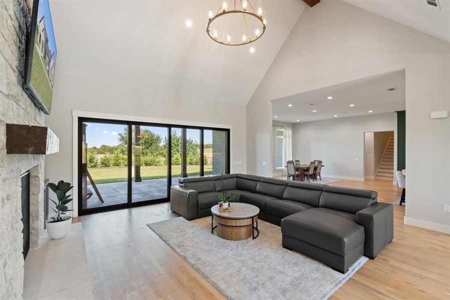 Living room featuring high vaulted ceiling, a fireplace, a notable chandelier, and light hardwood / wood-style flooring