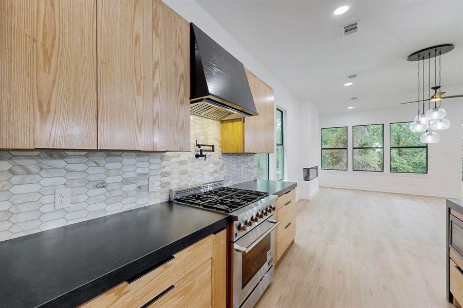 Modern kitchen featuring light wood-finish cabinetry, dark countertops, and a white hexagon tile backsplash Modern kitchen featuring light wood-finish cabinetry, dark countertops, and a white hexagon tile backsplash