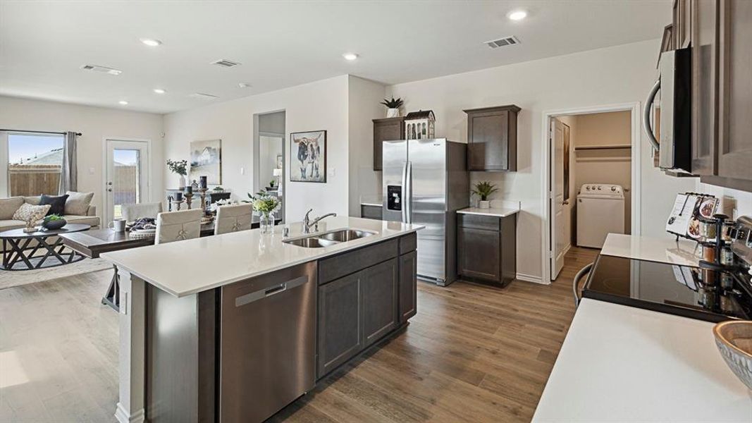 The kitchen features an island with a double basin sink and stainless steel dishwasher, dark wood cabinetry, white countertops, and wood-look flooring