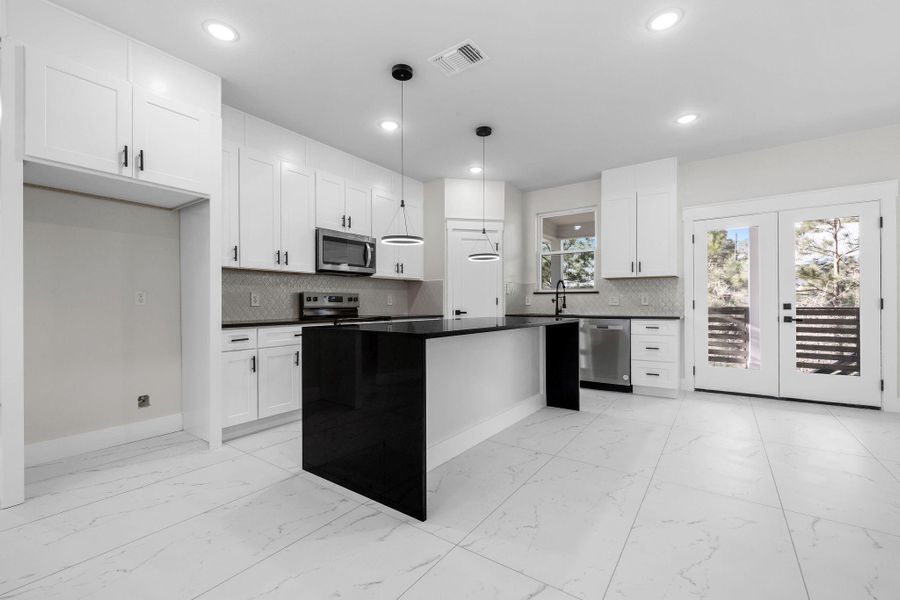 White cabinets, kitchen island,decorative light fixtures, backsplash, and stainless-steel appliances