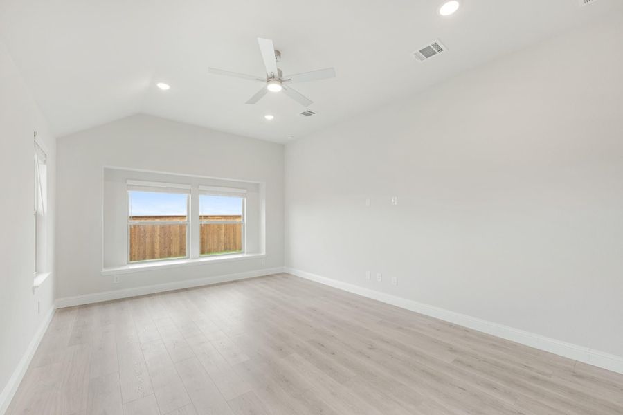 Empty bedroom with vaulted ceiling, ceiling fan, light wood floors, and backyard-facing window