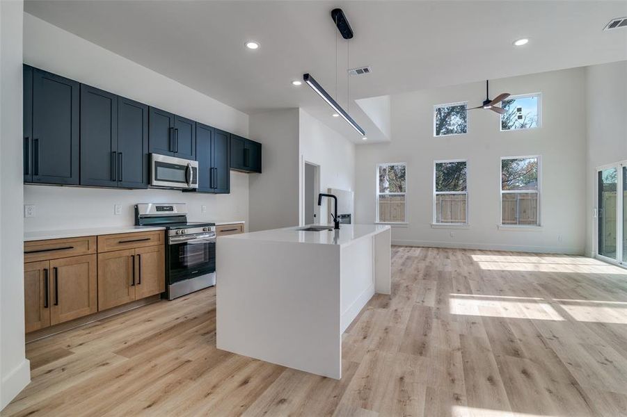 Kitchen with appliances with stainless steel finishes, light stone counters, a kitchen island with sink, a high ceiling, and recessed lighting