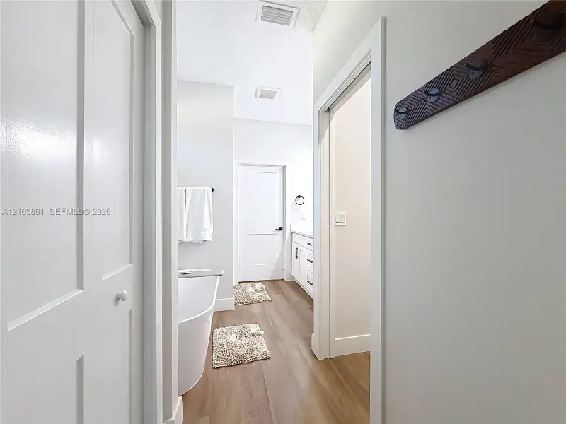 Bathroom featuring a freestanding soaking tub, white shaker-style cabinetry with neutral countertops, wood-finish flooring, and multi-panel interior doors