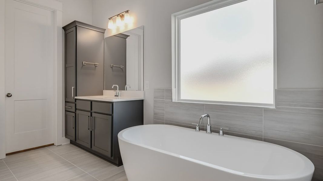 Large tiled bathroom with multiple vanities, glass shower enclosure, and freestanding tub